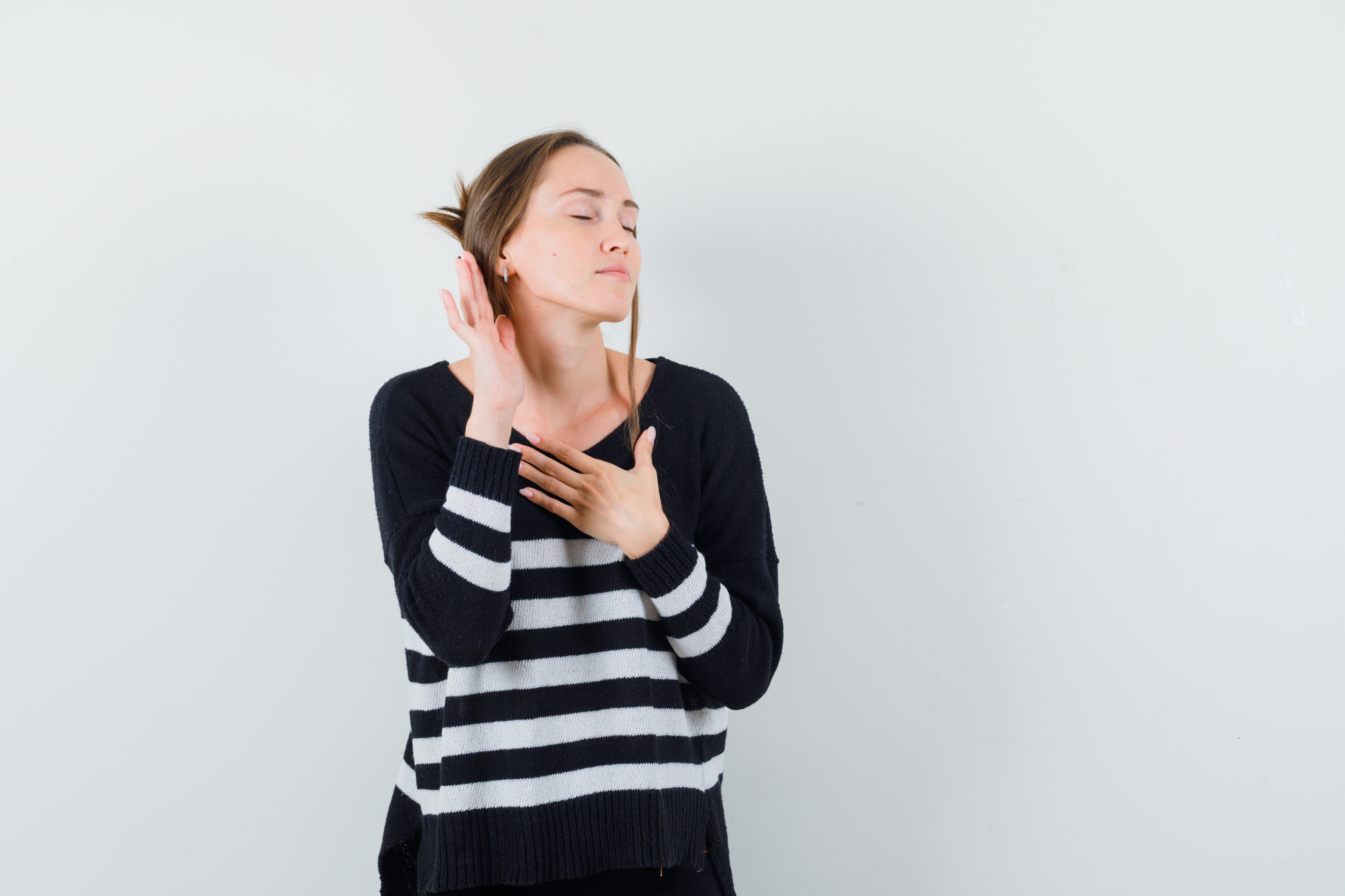 young-woman-standing-listening-pose-holding-one-hand-chest-while-closing-eyes-striped-knitwear-black-pants-looking-happy-3-_main